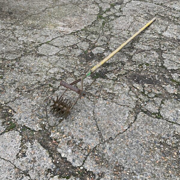 Long handle lawn aerator with spiked wheels and yellow timber handle on a paved surface