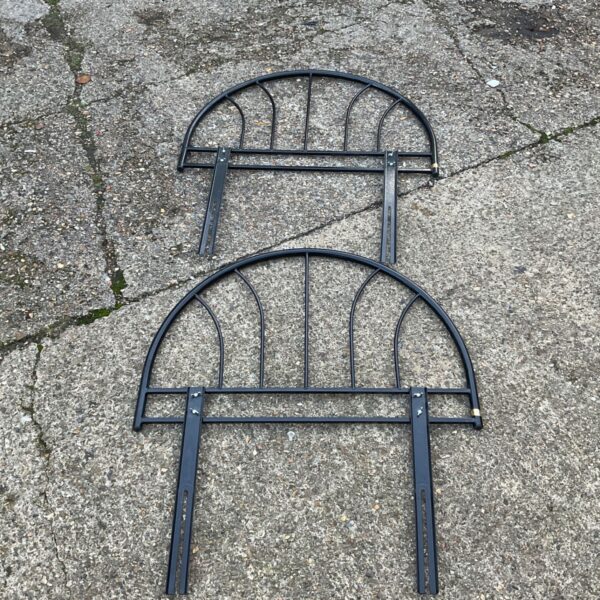 Pair of black metal arched headboards with vertical spindles on grey paving