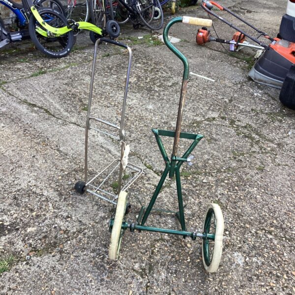 Vintage metal trolley frame with wheels in a garden setting.