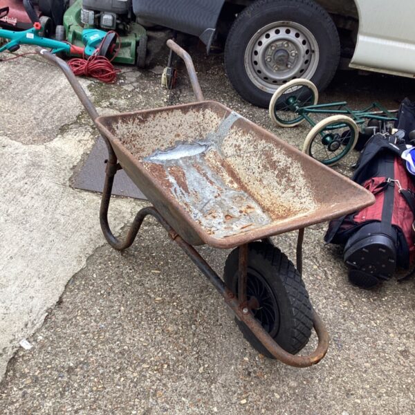 Rusty metal wheelbarrow with a pneumatic tyre in a garden setting.