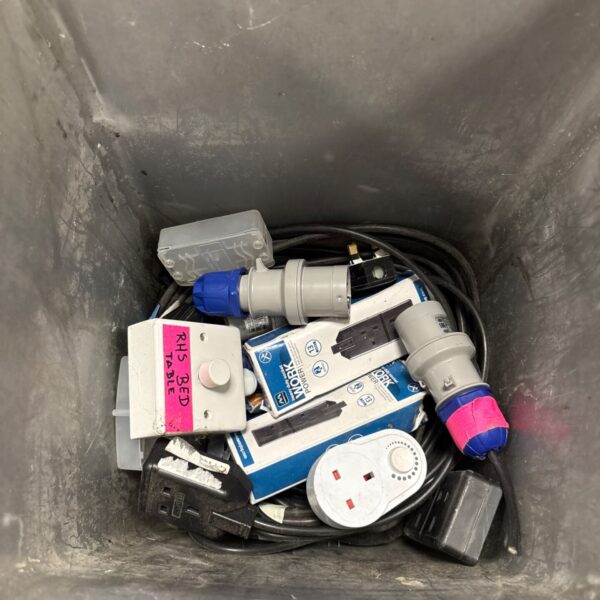 Grey box containing assorted electrical sockets, plugs, power strips and black leads