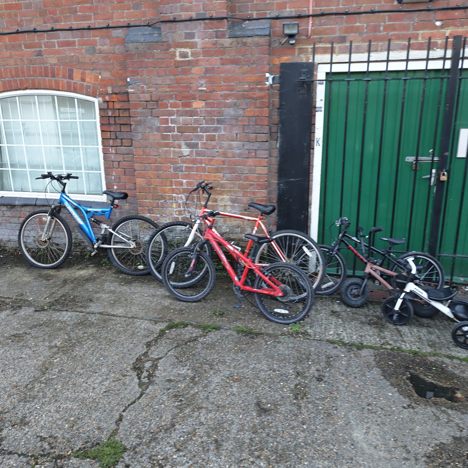 Mixed lot of six bicycles parked against brick wall and green gate