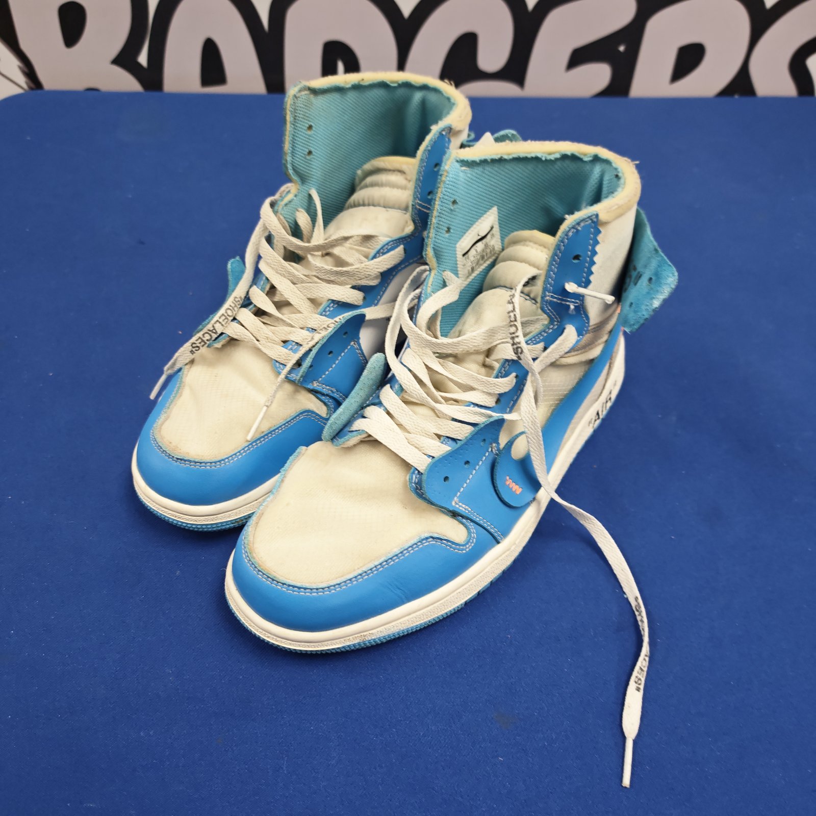 Pair of white and blue Nike Air style high-top trainers, size 9, on blue surface