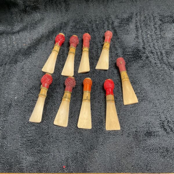 Nine cane bassoon reeds with red and orange thread-wrapped tops on dark fabric