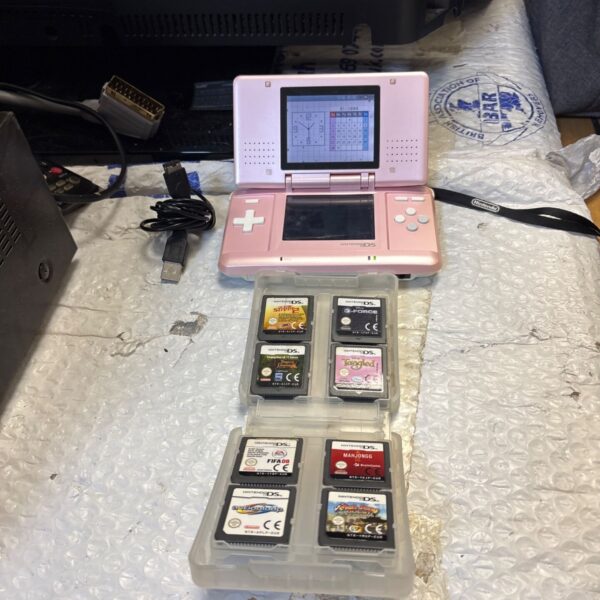 Pink Nintendo DS console with charger and twelve games displayed.