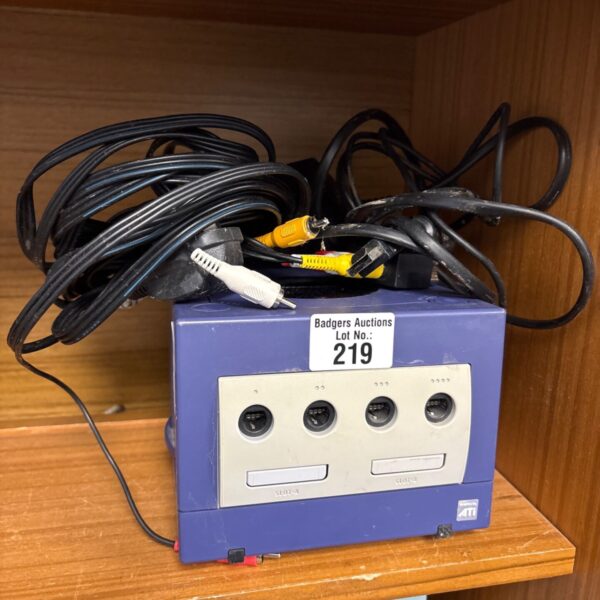 Purple Nintendo GameCube console with black and yellow cables on wooden shelf
