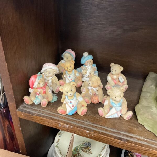 Collection of P Hillman teddy bear figurines in pastel costumes on wooden shelf