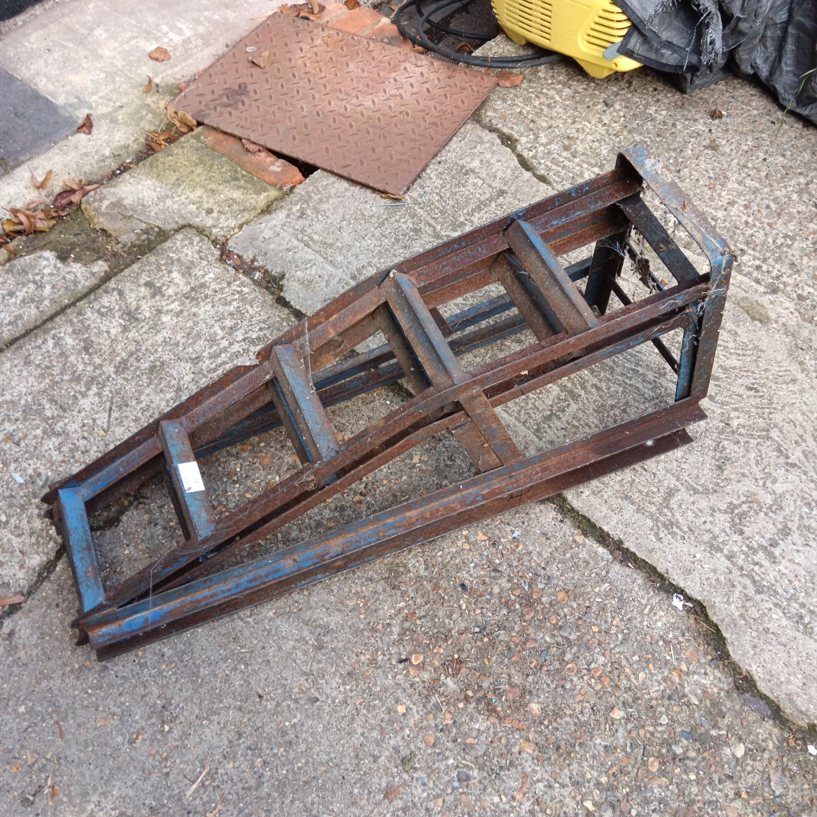Pair of rusted metal car ramps with blue paint remnants on a paved surface
