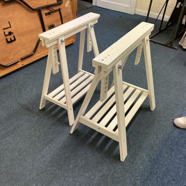 Pair of white painted wooden trestles with slatted lower shelves on carpet