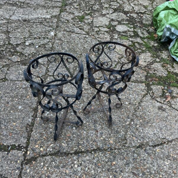 Pair of scrolled wrought iron plant stands with twisted legs on paving