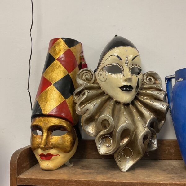 Two colourful papier mache masquerade masks displayed on a shelf.