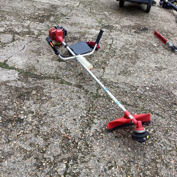 Red petrol garden strimmer with silver shaft and circular cutting head on paving