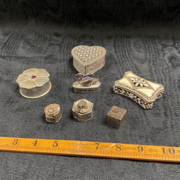 Group of pewter trinket boxes including heart, flower and swan designs on dark fabric
