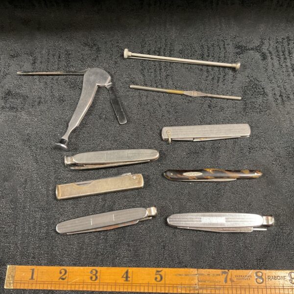 Collection of pipe cleaning pocket tools and folding pocket knives on dark fabric