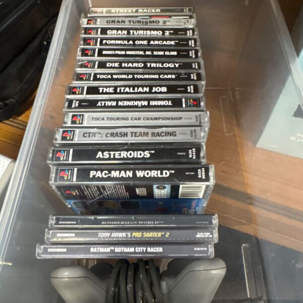 Stack of PlayStation 1 game cases with grey controller and cable