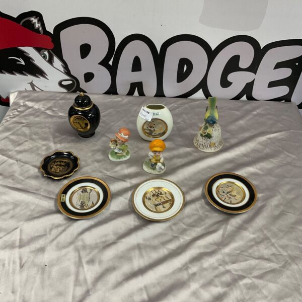Collection of porcelain figurines, black and gold ginger jar and decorative plates on grey cloth