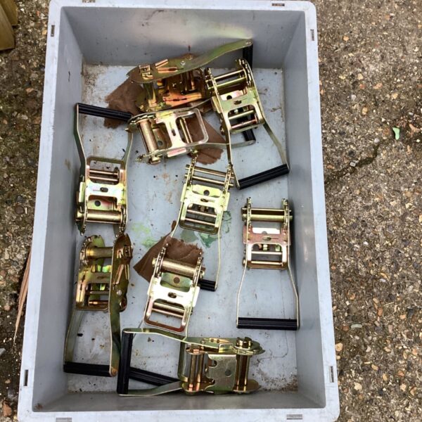 Box of yellow zinc-plated ratchet clamps with black rubber handle grips in grey crate