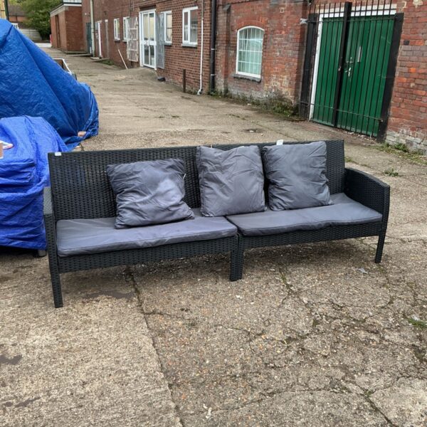 Grey cushioned rattan garden sofa on a paved patio.