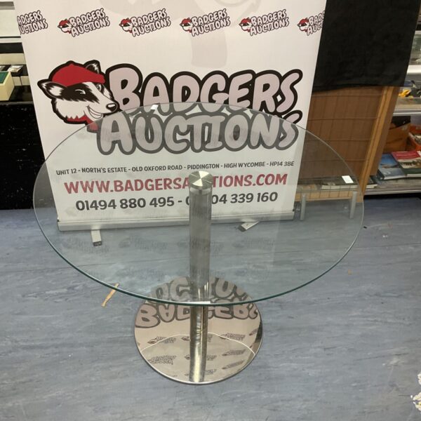 Round glass table with a pedestal base, showing minor wear.