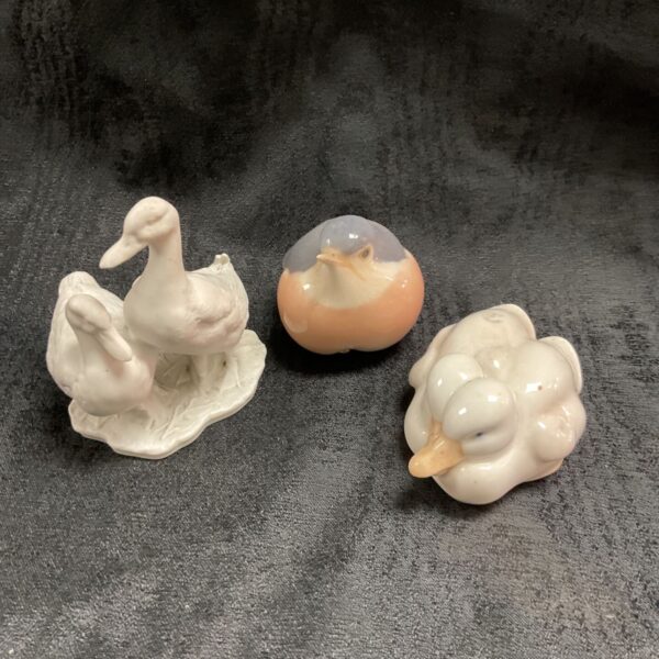 Royal Copenhagen robin, white ducks and Kaiser geese porcelain figurines on dark fabric