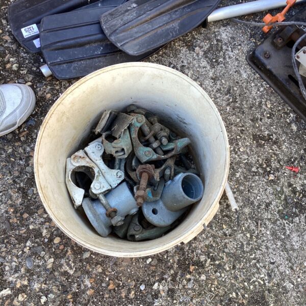 Bucket of used metal scaffolding clamps for construction projects.