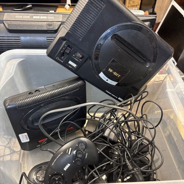 Two black Sega Mega Drive consoles with controllers and tangled power cables