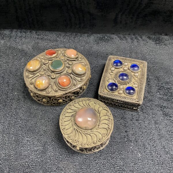 Three white metal filigree trinket pots with cabochon-set lids on a dark surface