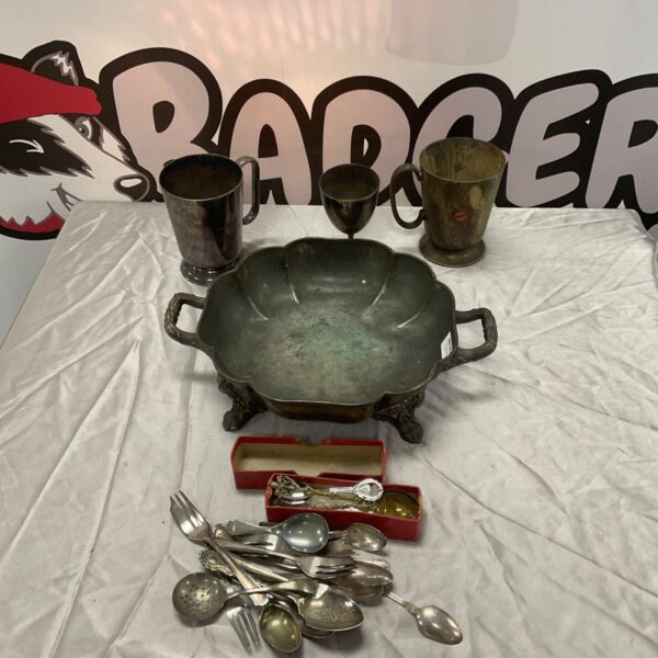 Silver plated fruit bowl, tankards, goblet and flatware arranged on white cloth