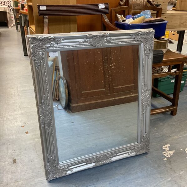 Silver tone framed wall mirror with ornate moulded scrolling frame