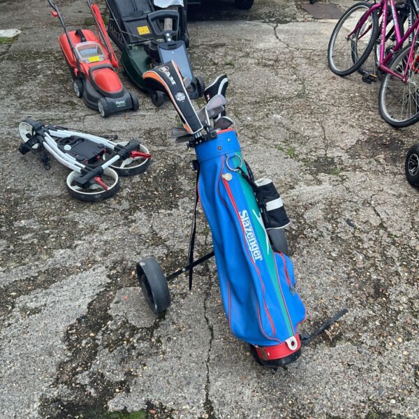 Blue Slazenger golf bag with clubs and wheeled trolley on concrete