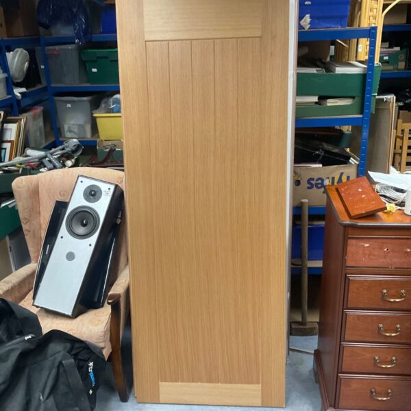 Light oak panelled door with vertical grooves standing upright against a wall