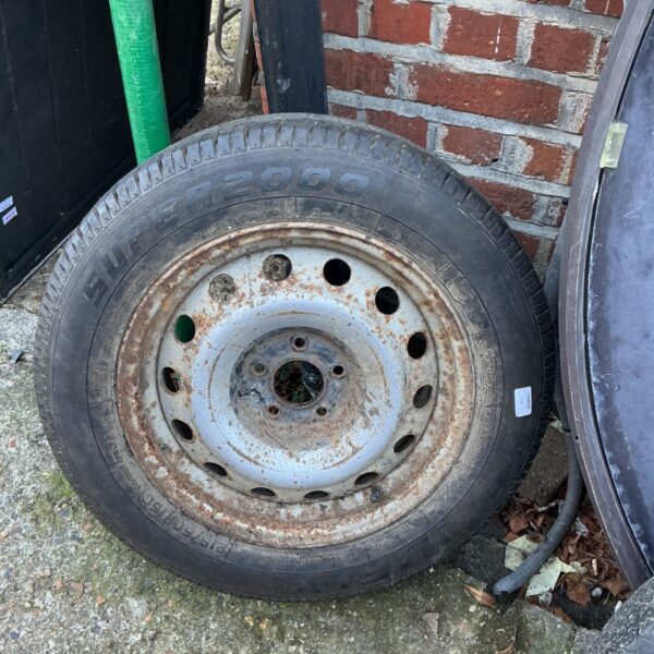 Spare trailer tyre 215/60R on rusted pressed steel wheel, standing outdoors