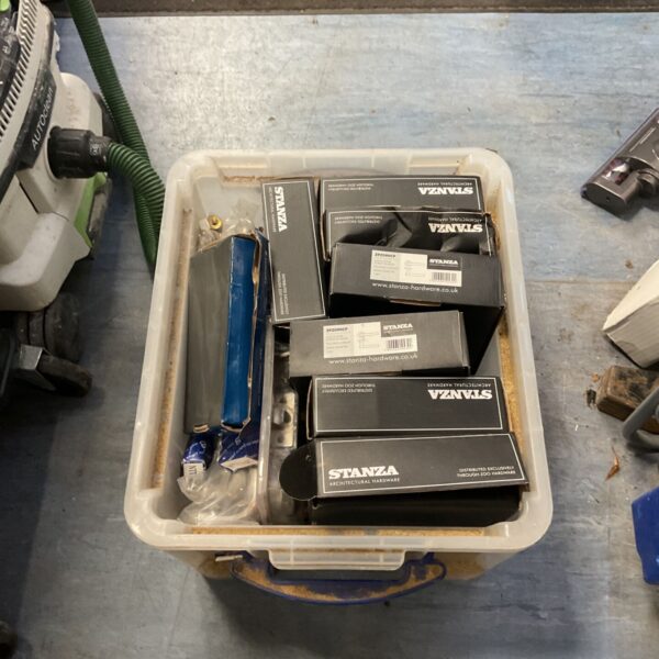 Crate of boxed Stanza lever door handles and mixed door hardware on a workshop floor