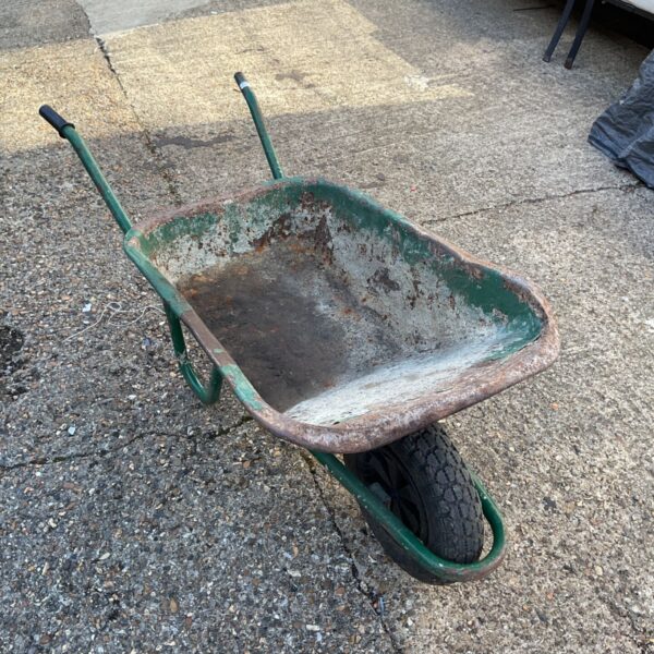 Weathered steel garden wheelbarrow in a garden setting.