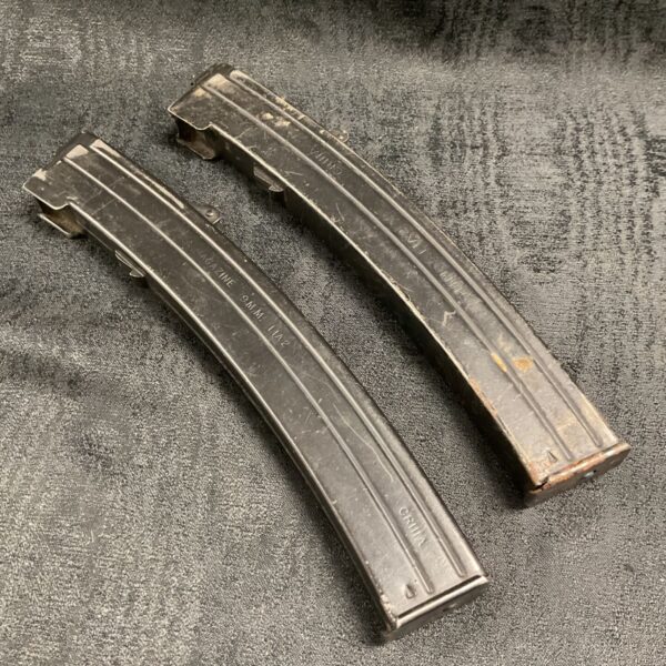 Pair of black metal 34 round 9mm Sterling SMG magazines on grey fabric