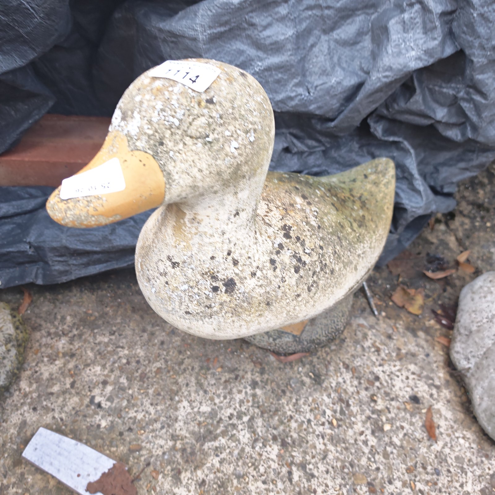 Weathered stone duck garden statue with orange-yellow bill and lichen staining