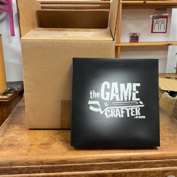 Black box with white The Game Crafter logo beside an open cardboard carton