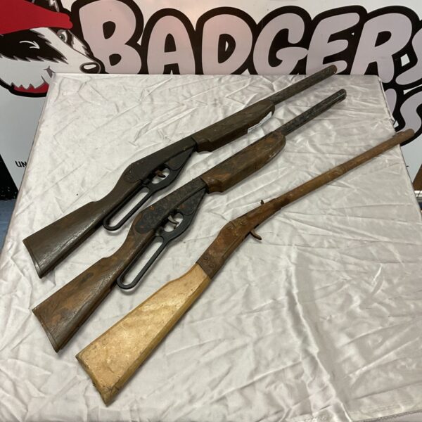 Three vintage children's toy rifles with wooden stocks, one a Daisy, on a white cloth.