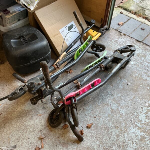 Three black folding scooters with pink and green footboards on a concrete floor