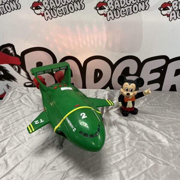 Green plastic Thunderbirds 2 toy ship beside a Mickey Mouse coin bank