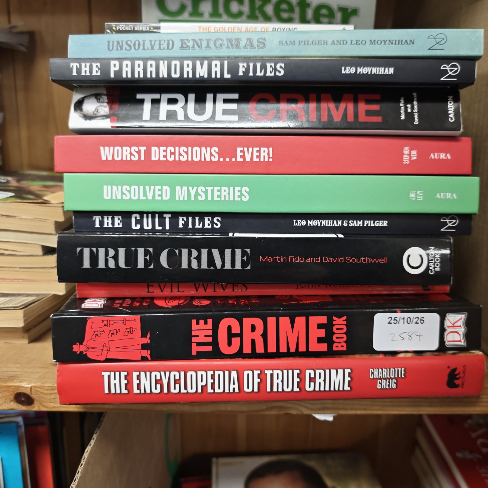 Stack of true crime and unsolved mysteries books on wooden shelf