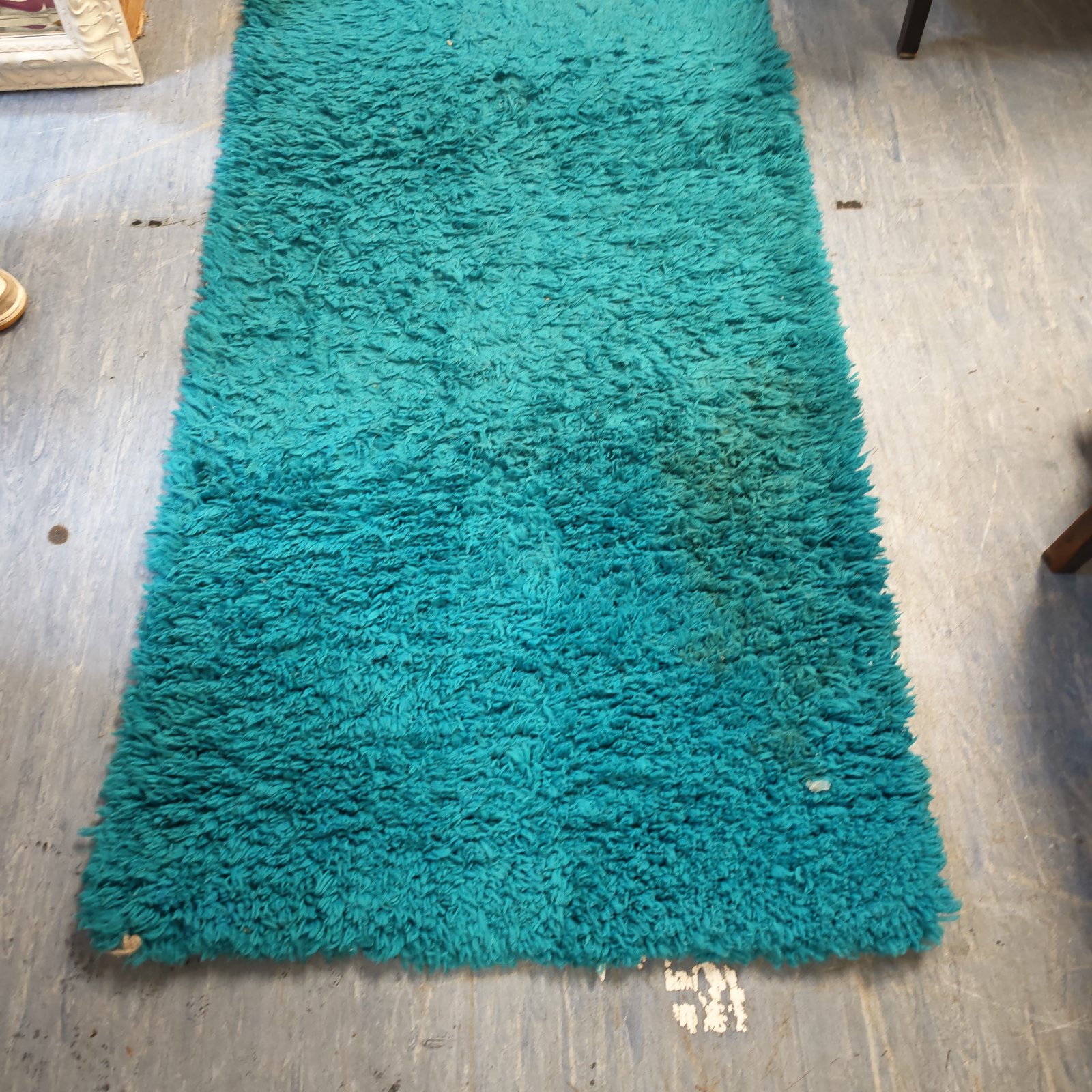 Turquoise shag pile rug laid flat on a grey wooden floor