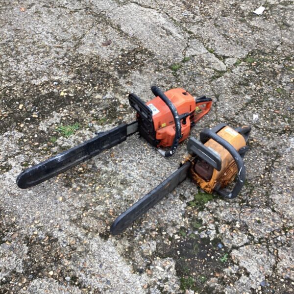 Two petrol chainsaws with orange and yellow bodies on a concrete surface