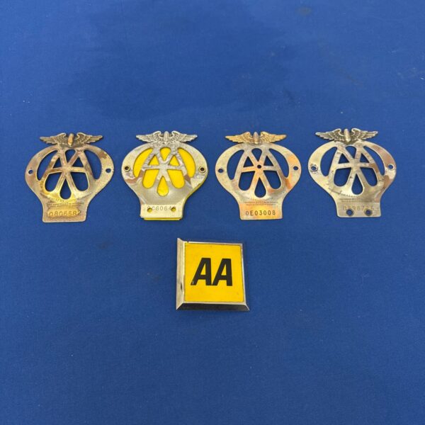 Five vintage AA car grille badges laid out on a blue surface
