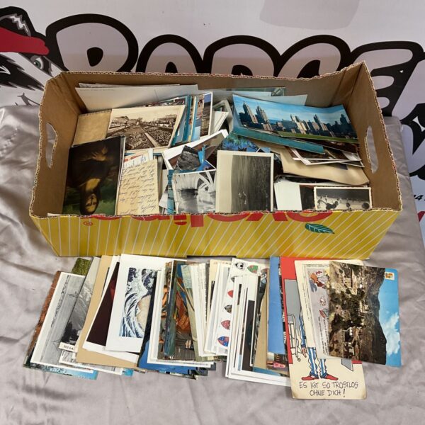 Mixed lot of vintage and antique postcards in a cardboard box with more laid out below