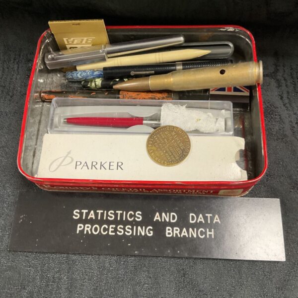 Vintage tin of assorted pens with red Parker ballpoint and brass practice bullet