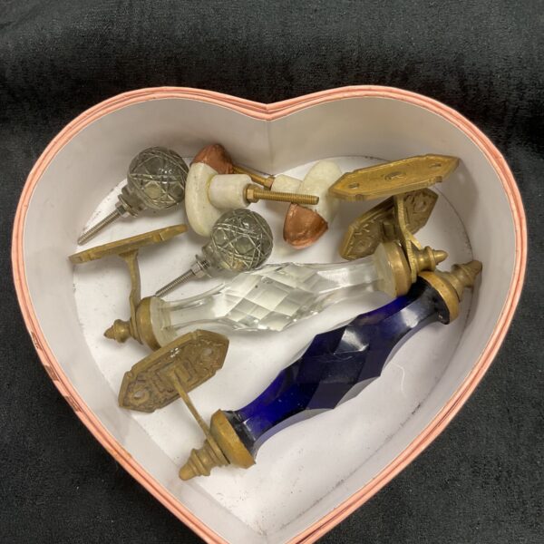 Vintage brass and glass handles displayed in a heart-shaped box.