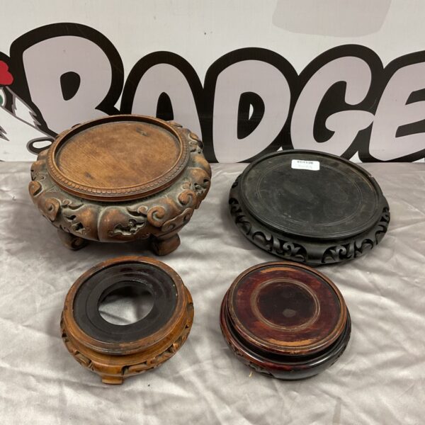 Four vintage carved wood Chinese pot stands arranged on a grey fabric surface