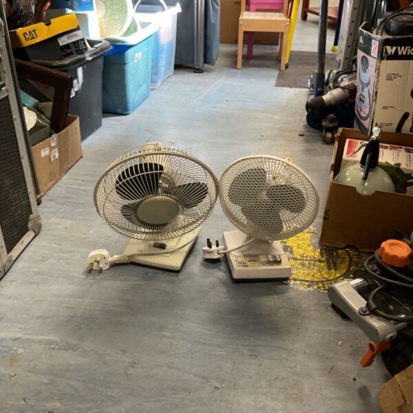 Pair of vintage desk fans on a workshop floor.