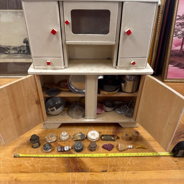 Vintage dollhouse kitchen cabinet with open door and accessories.